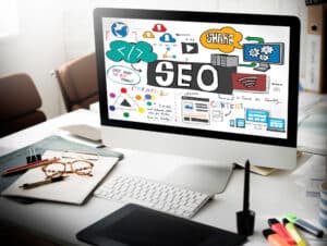 Computer monitor displaying SEO concepts and graphics, surrounded by office supplies, symbolizing digital marketing strategies for small businesses.